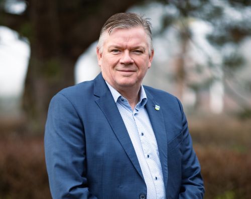 Morten Dahlberg, borgmesterkandidat for Socialdemokratiet i Gribskov, står udendørs i en blå habitjakke og lys skjorte. Han er engageret i lokalpolitik og stiller op til kommunalvalget i Gribskov Kommune.